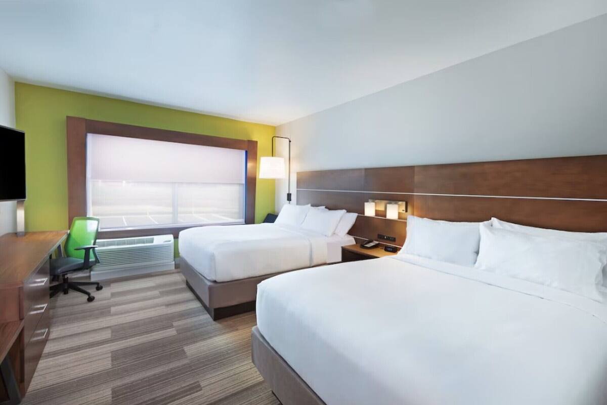 A hotel room with two beds, a desk, a chair, a TV, and a window with blinds.