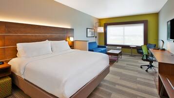 A hotel room with a large bed, a desk, a chair, a sofa, and a window with a view.