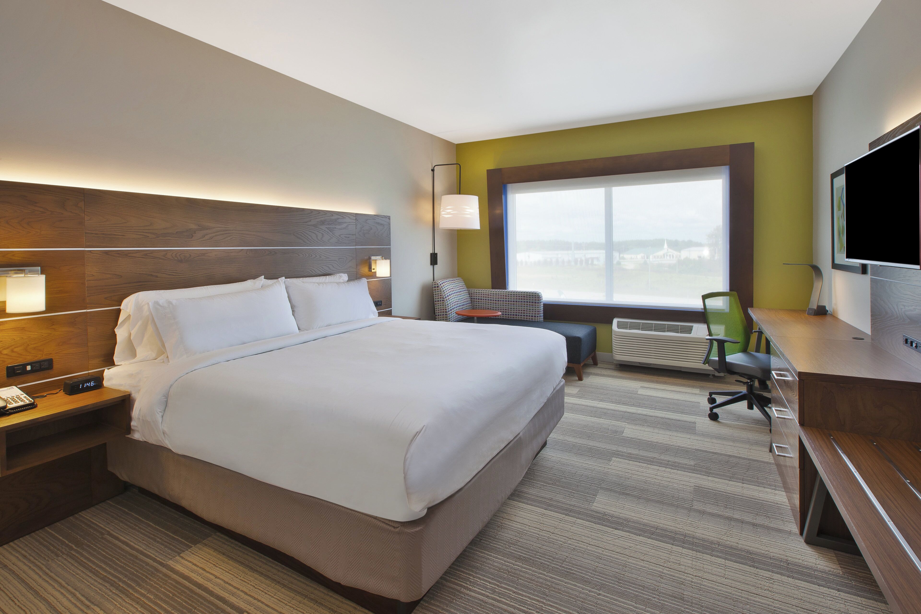 A hotel room with a large bed, a desk, a chair, a TV, and a window with a view.