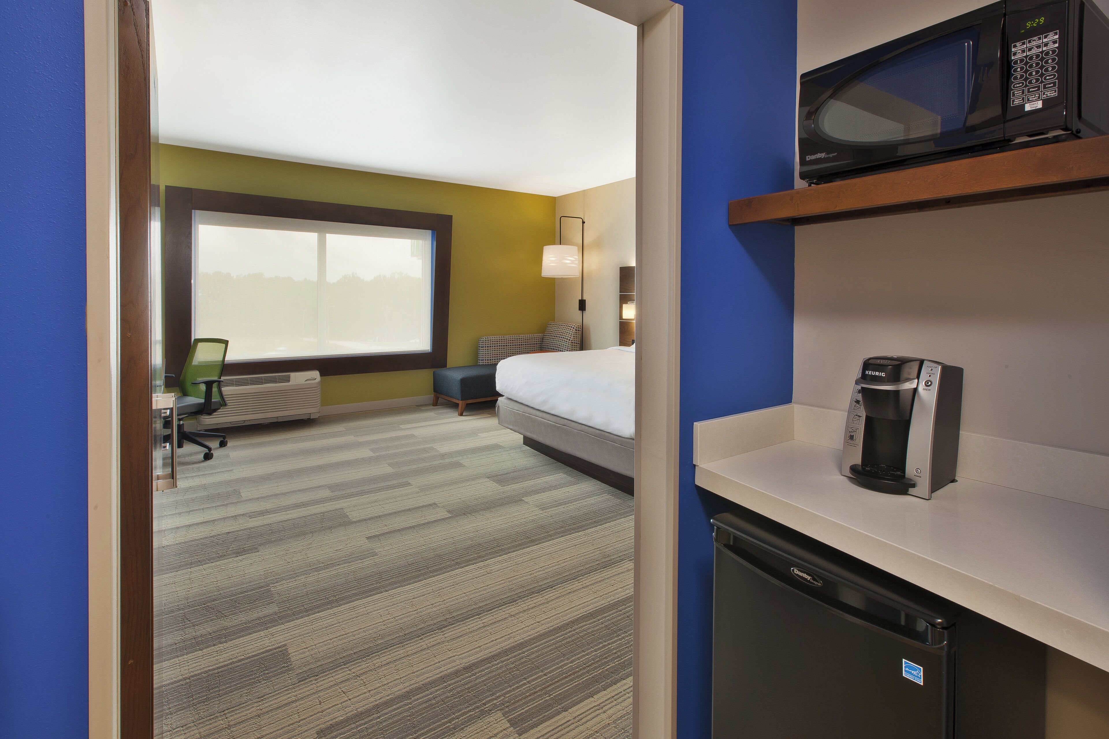 A hotel room with a bed, a microwave, a coffee maker, a desk, and a chair.