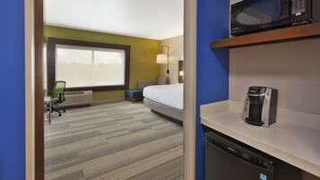 A hotel room with a bed, a microwave, a coffee maker, a desk, and a chair.