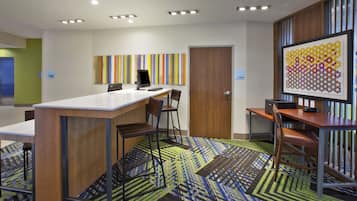 A modern office space with a long table, chairs, a computer, and a colorful abstract painting.