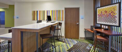A modern office space with a long table, chairs, a computer, and a colorful abstract painting.