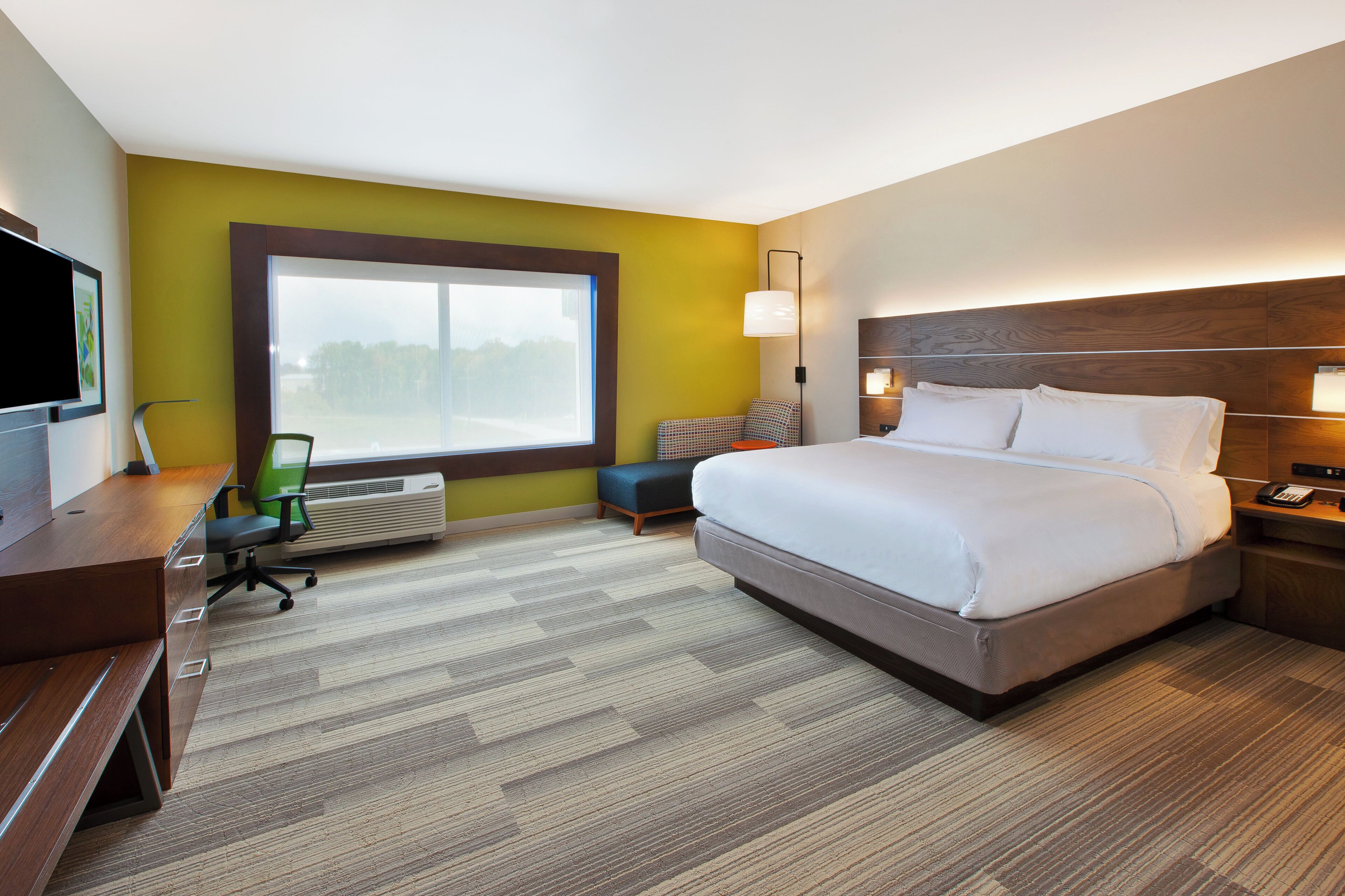 Une chambre d’hôtel avec un grand lit, un bureau avec une chaise, une télévision et une fenêtre donnant sur un beau paysage.