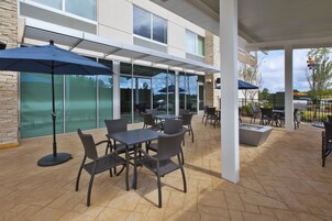Un área de patio al aire libre con mesas y sillas, cubierta por una estructura de techo.