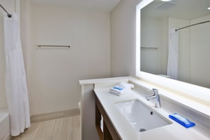 Un baño moderno con un lavamanos blanco, un espejo y una cortina de ducha.