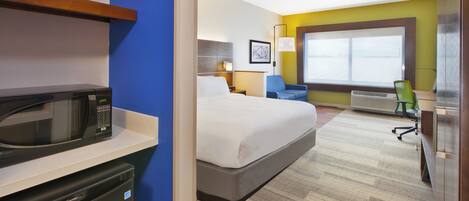 A hotel room with a bed, a desk, a chair, a microwave, and a small refrigerator.