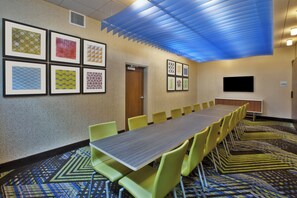 A conference room with a long table and chairs, framed artwork on the walls, and a television on the wall.