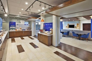 A modern kitchen area with a central island, a dining area with blue chairs, and a bakery section with pastries.
