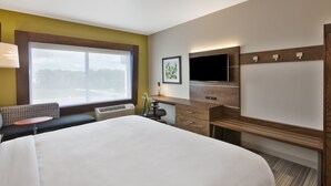 A hotel room with a large bed, a desk with a flat-screen TV, a bench, and a window with a view of trees. - Holiday Inn Express & Suites South Hill by IHG (South Hill)