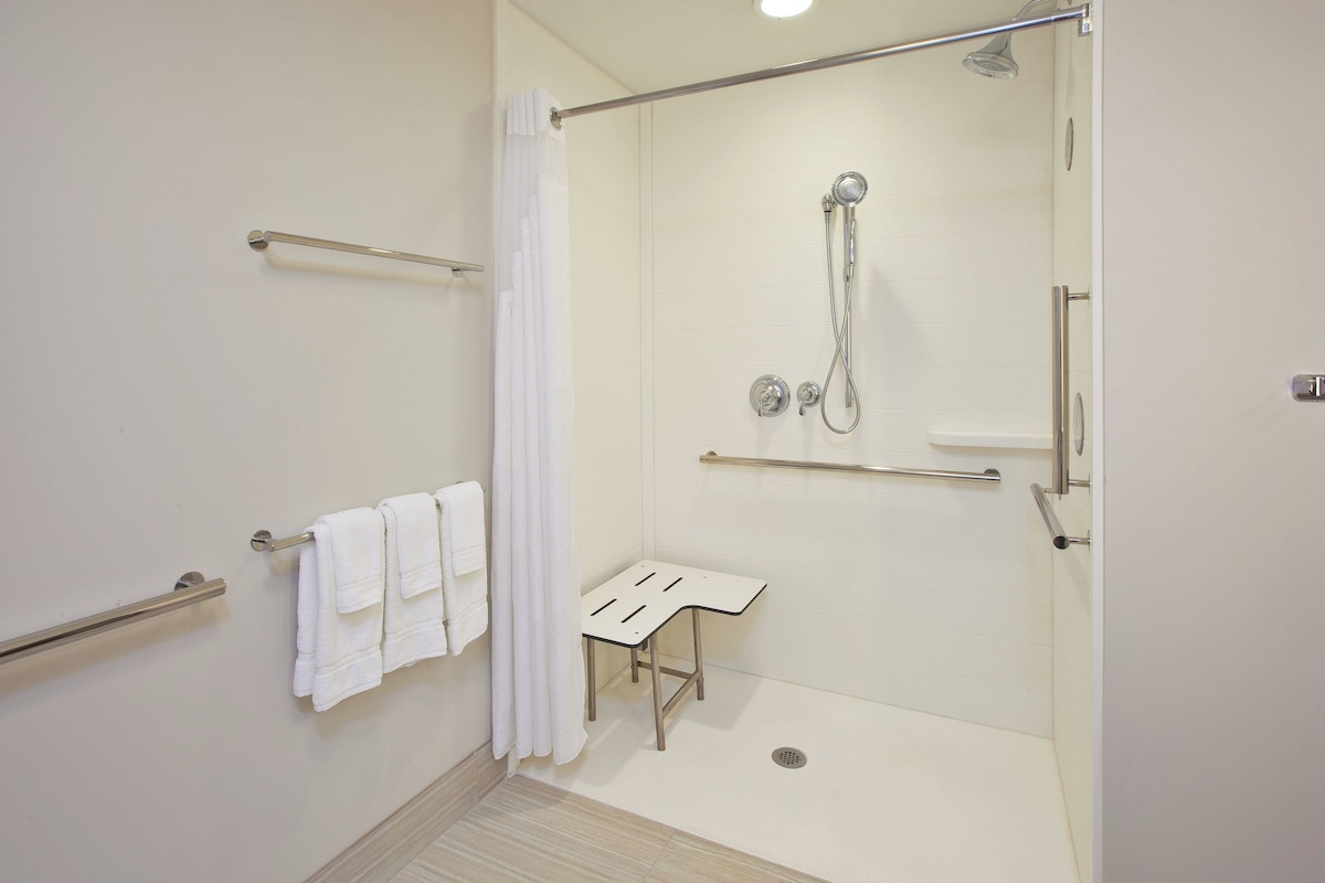 Un baño moderno con ducha, perchero, una mesita pequeña y baranda.