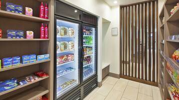 Un expositor refrigerado con diversos alimentos y bebidas, un estante con productos de higiene personal y una partición de madera.