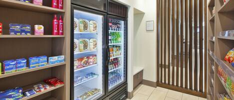 A refrigerated display with various food items and beverages, a shelf with personal care products, and a wooden partition.