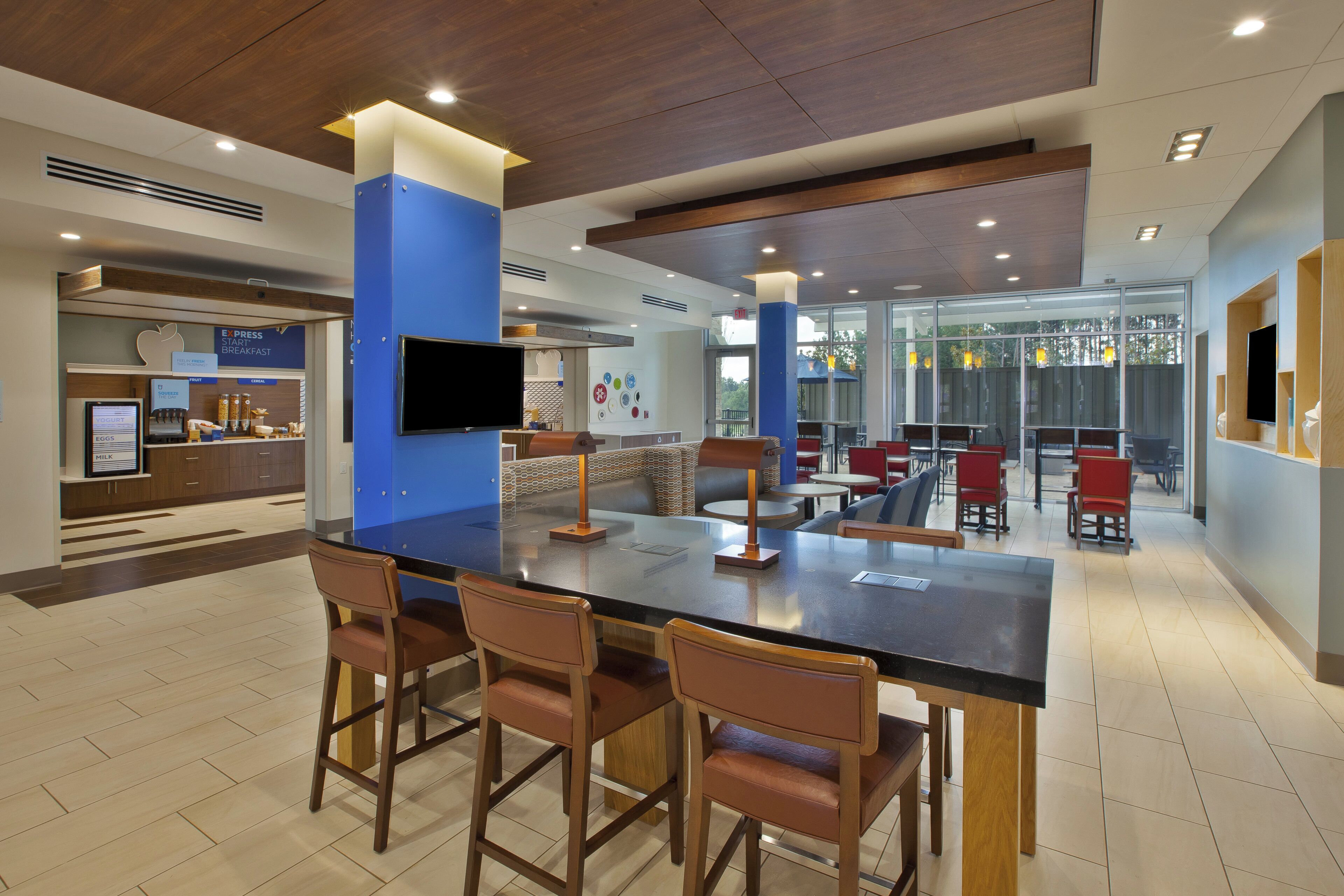 A modern hotel lobby with a central bar area, seating arrangements, and a breakfast counter.