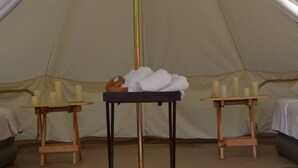 Une tente avec une table sur laquelle sont posées des serviettes et des bougies, deux petites tables en bois et un lit avec une couverture.