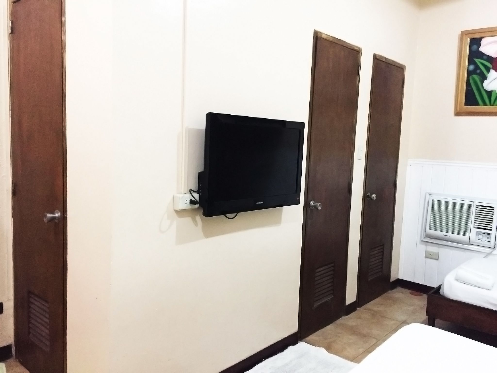 A hotel room with a TV mounted on the wall, a radiator, and a bed with a white cover.