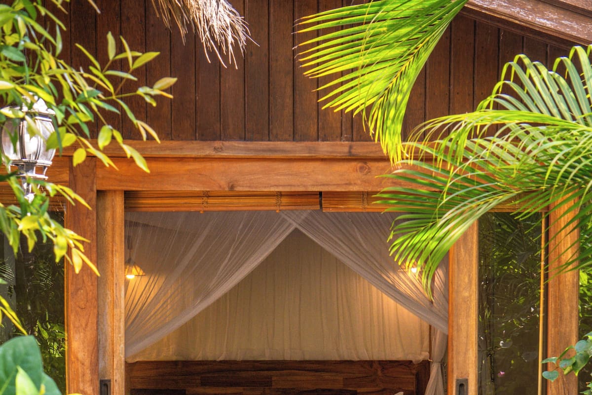 A wooden bed with a canopy, surrounded by plants and a stone pathway.
