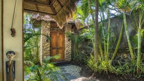 A stone building with a wooden door, surrounded by tropical plants and a stone wall. - Breezy Point Villas (Nusa Dua)