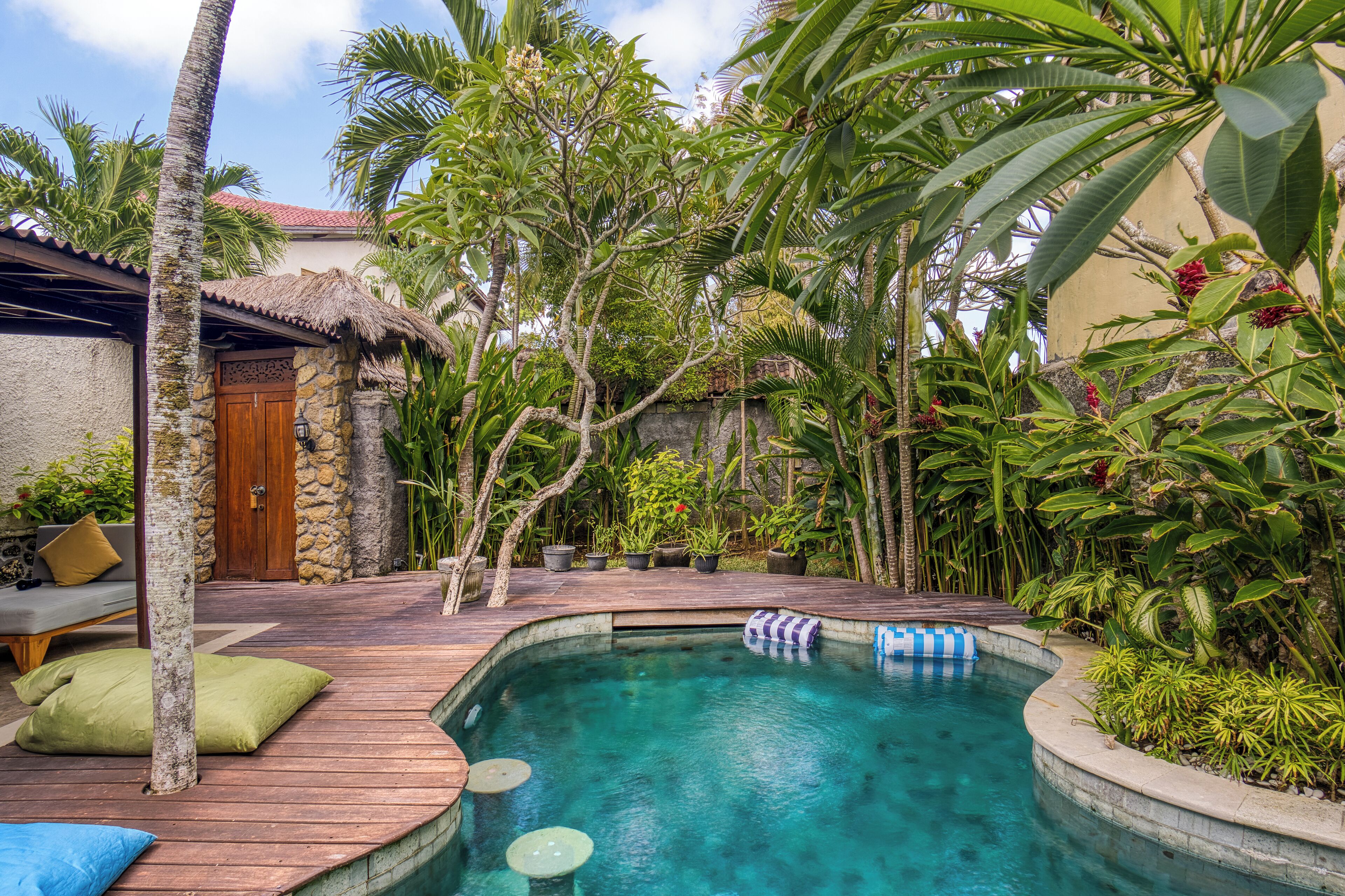Un área de piscina con terraza de madera, sillones de descanso y plantas tropicales.