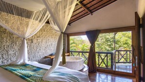A room with a bed, a stone wall, a large window, and a balcony. - Breezy Point Villas (Nusa Dua)