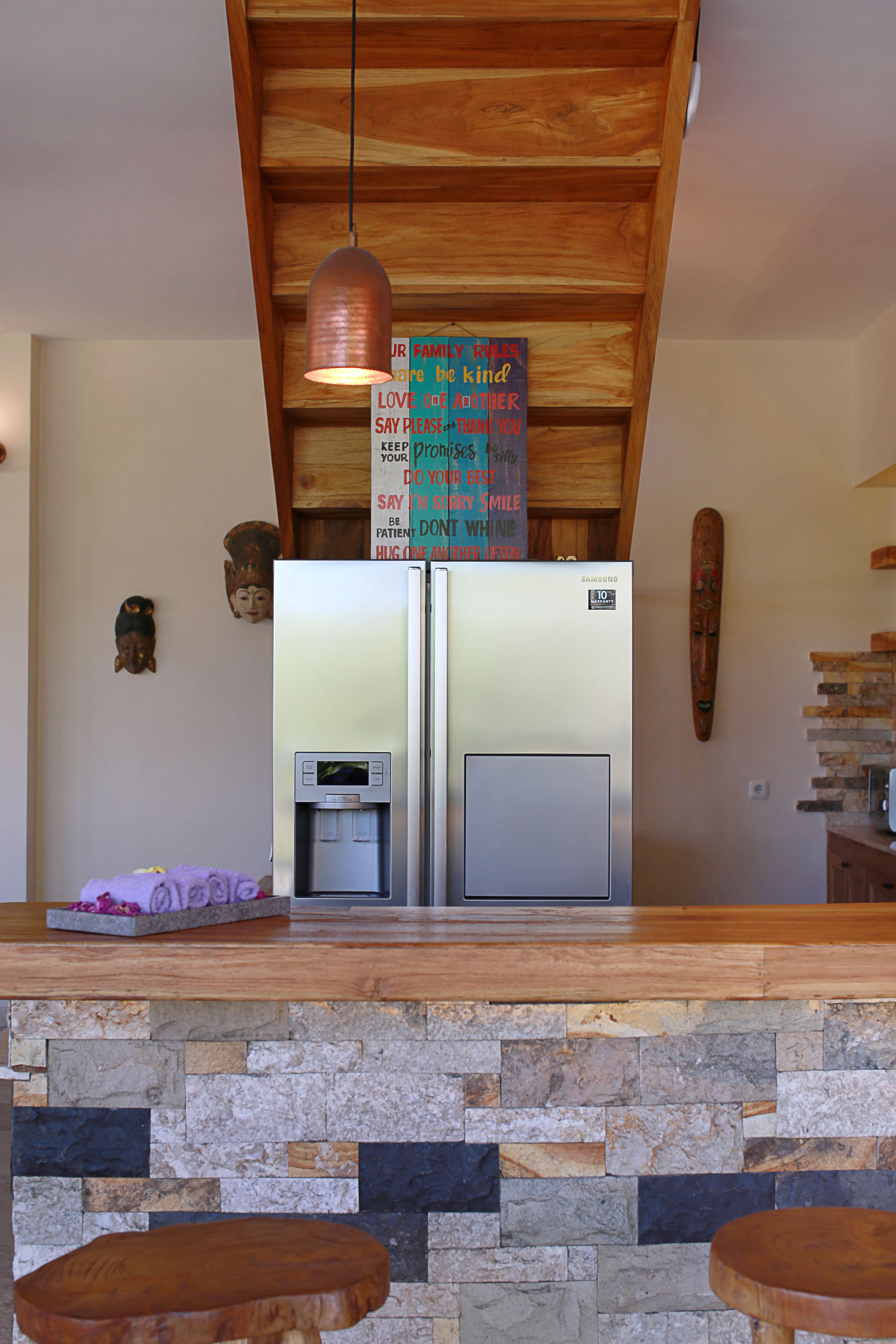 A modern kitchen with a stone backsplash, a stainless steel refrigerator, and a wooden ceiling.