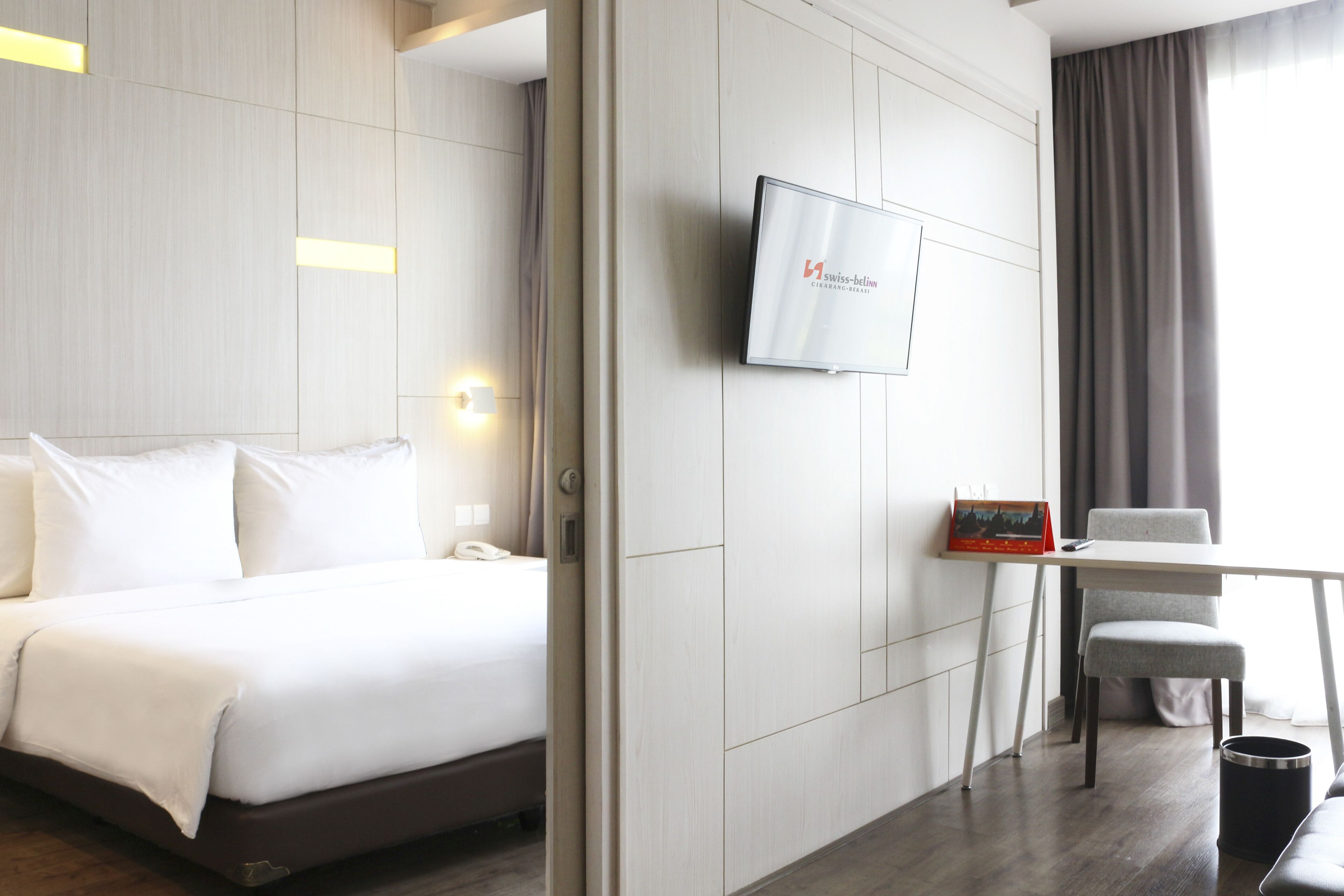 Una camera d'albergo moderna con un letto, una scrivania, una sedia e una televisione appesa al muro.