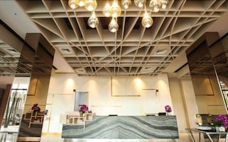 Um balcão de receção com bancada de mármore, um design de teto moderno com luzes pendentes e uma disposição simétrica.