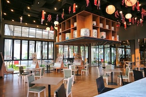 Um espaço interno amplo, com várias mesas e cadeiras, janelas grandes e prateleiras com objetos decorativos.