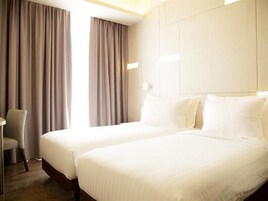 A hotel room with two beds, a chair, and a large window with curtains.