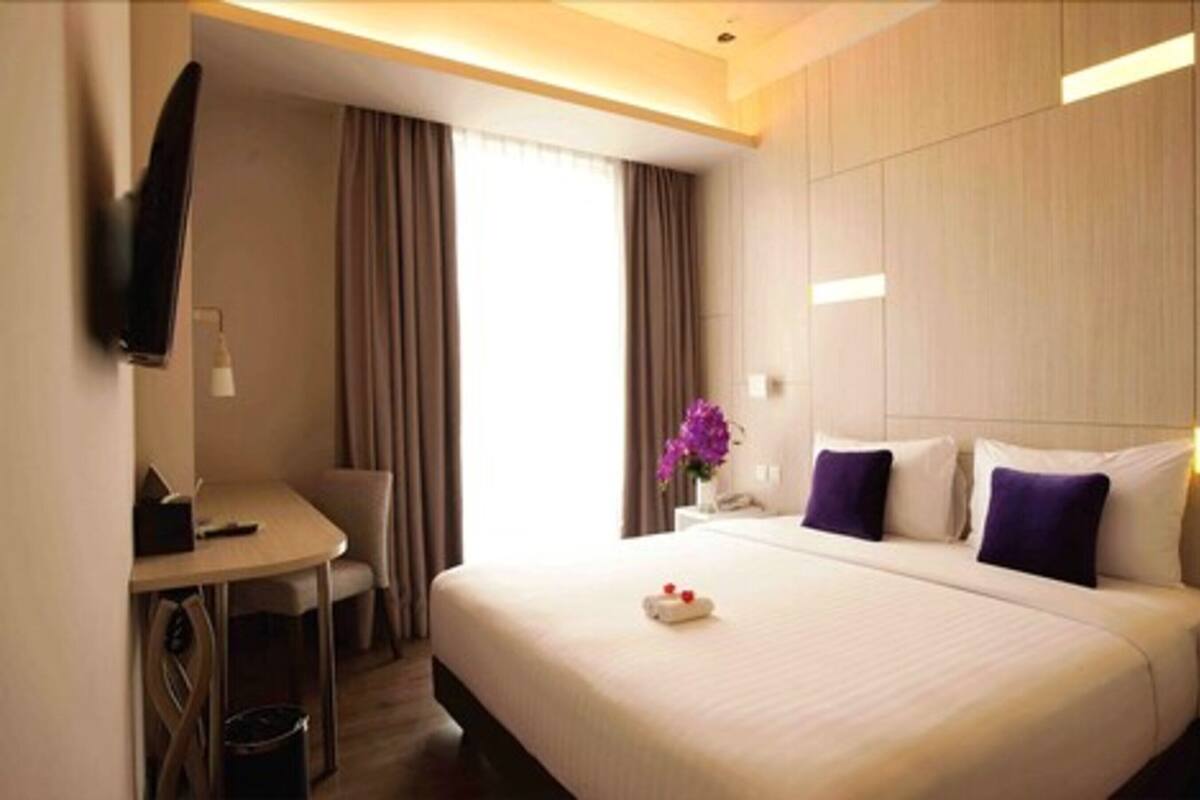 Ein Hotelzimmer mit Bett, Schreibtisch, Stuhl, Fernseher und einem Fenster mit Vorhängen.