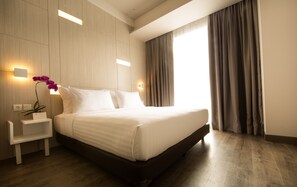 Un hotel moderno con una cama grande, paneles de madera, una mesita de noche, una orquídea en maceta y vistas al exterior a través de una ventana con cortinas.