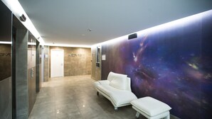 A modern lobby with a white sofa and bench, a hallway with elevators, and a wall with a space-themed mural. - Nova Mooloolaba Beach (Mooloolaba)