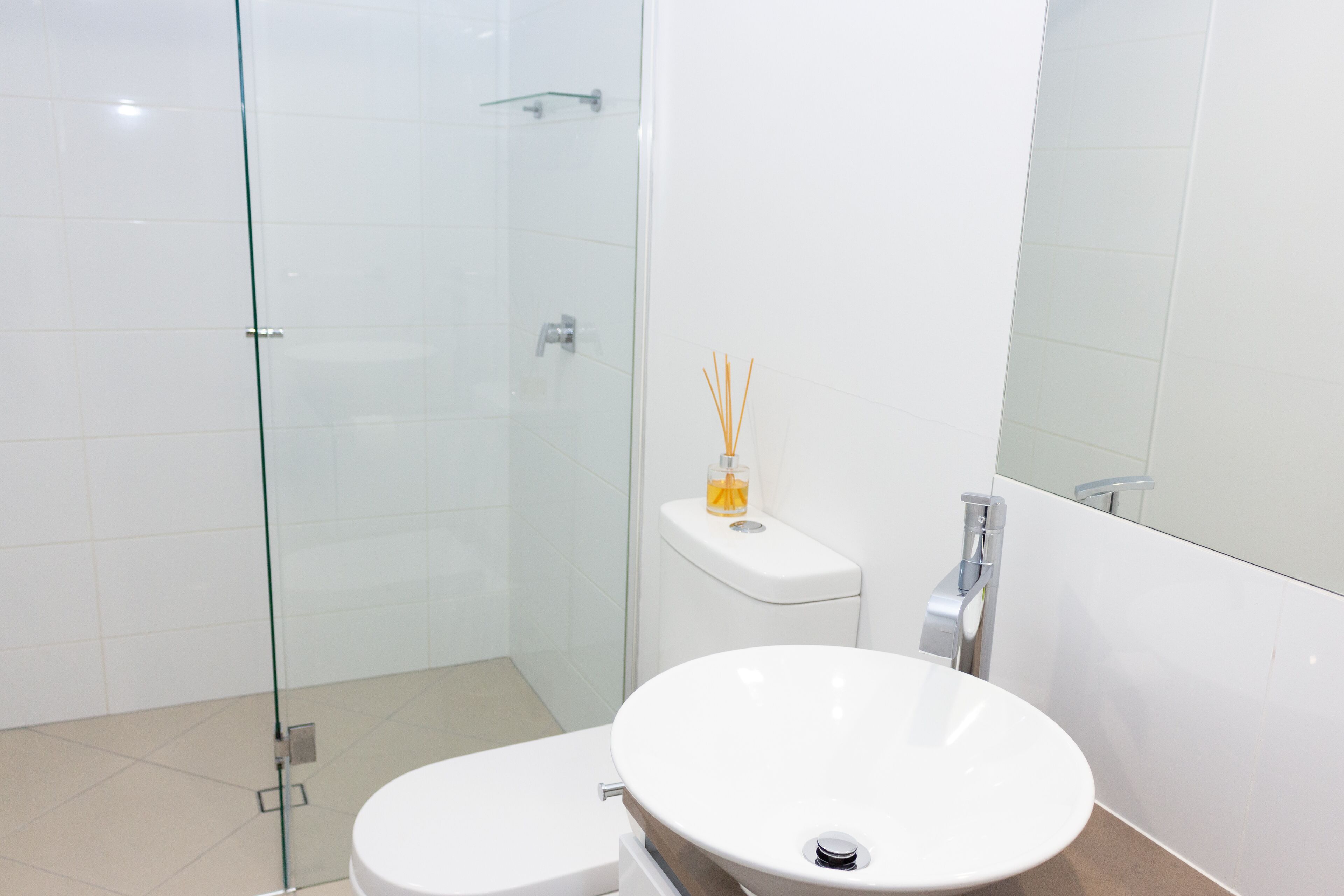 A modern bathroom with a glass shower enclosure, a white toilet, and a round sink with a mirror above it.