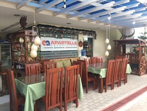 Un área de comedor al aire libre con mesas y sillas de madera, un letrero que dice 'Caff. Partelle' y un techo decorativo.