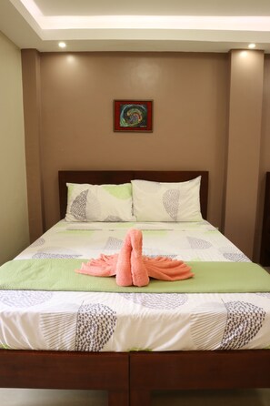 Una cama bien hecha con una colcha verde y blanca estampada, dos almohadas con diseños de hojas y un cuadro decorativo en la pared de arriba.