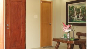 Une pièce avec une porte en bois, une petite table sur laquelle est posé un vase de fleurs et un tableau encadré accroché au mur.