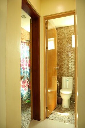 Un baño con inodoro, cortina de ducha y pared de mármol.