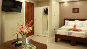Une chambre d’hôtel avec un lit, un téléviseur fixé au mur, une armoire et un bureau agrémenté d’un vase de fleurs.