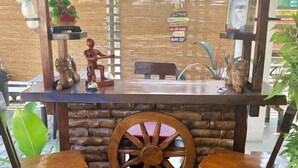 Un espace extérieur rustique aménagé avec une table en bois, une roue décorative et divers objets disposés sur des étagères.