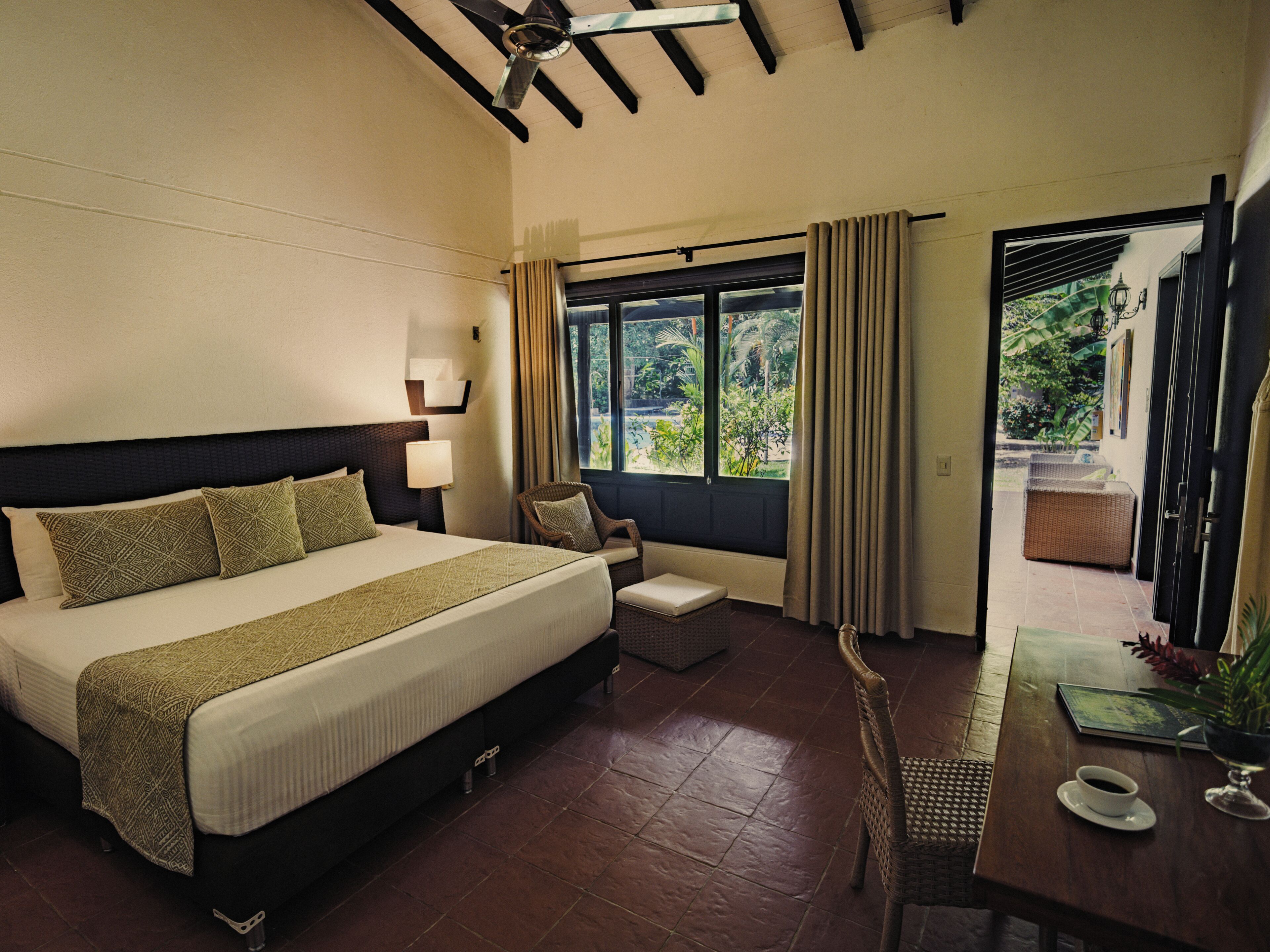 Quarto de hotel com cama, uma cadeira, mesa com xícara e vista para o exterior.