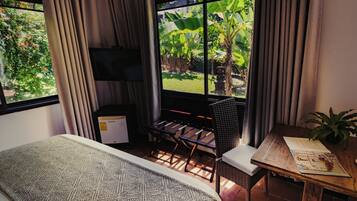 Un dormitorio con una cama, un escritorio, una silla, un televisor y una ventana con cortinas.