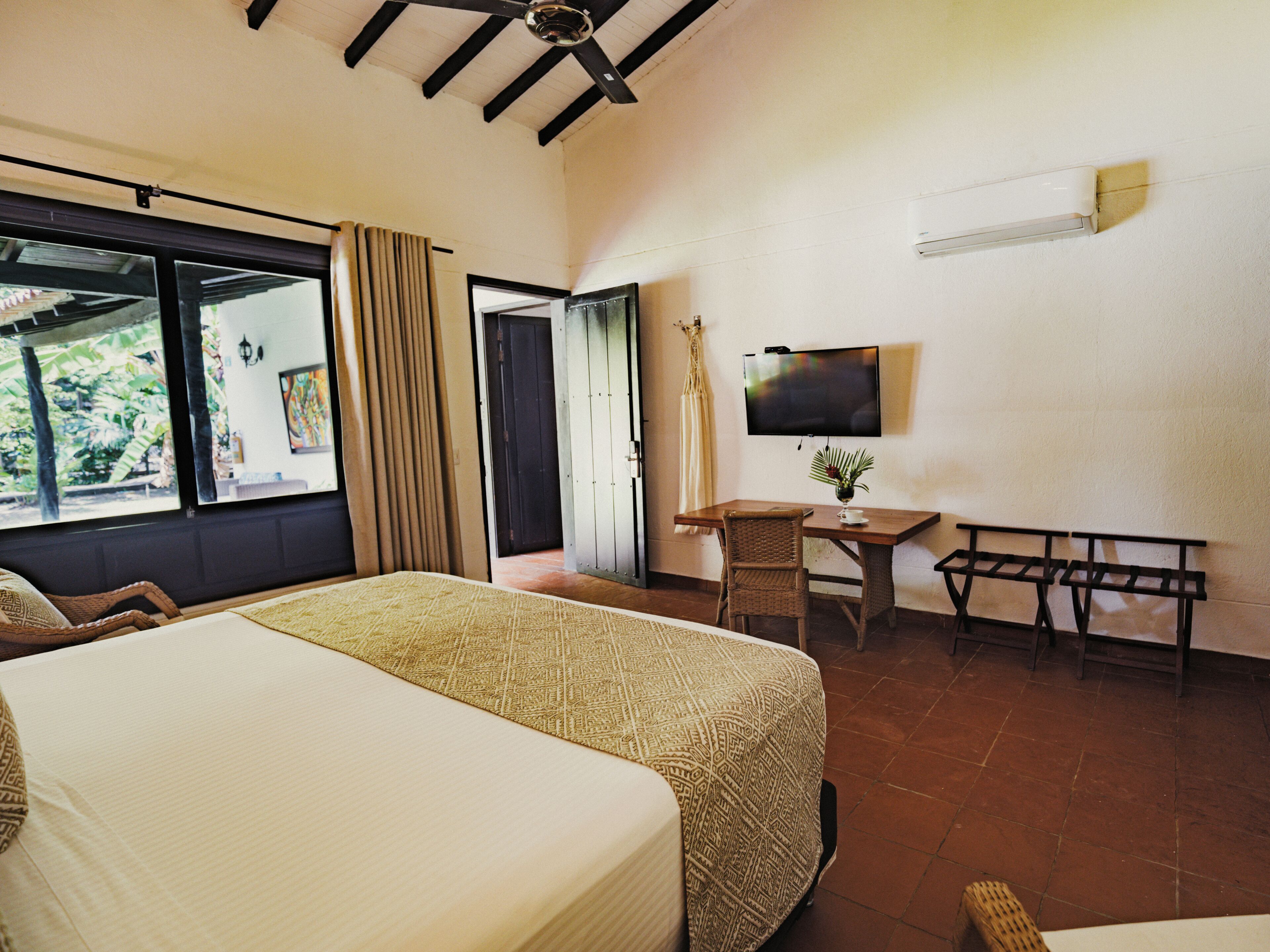 A hotel room with a large bed, a desk with a chair, a television, and a window with curtains.