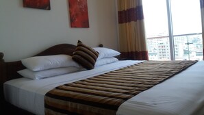 A hotel room with a large bed, a view of the city through a window, and two abstract paintings on the wall. - Colombo Sea View Apartment (Colombo)