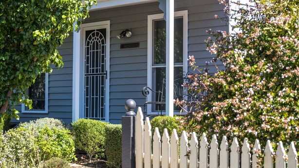 A house with a picket fence, a window with a decorative grille, and a small porch area. - Birdie (Daylesford)