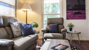 A living room with a sofa, armchair, lamp, small table, and a painting on the wall. - Birdie (Daylesford)
