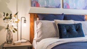 A neatly arranged bedroom with a wooden headboard, a bedside table with a lamp, and a vase with flowers. - Birdie (Daylesford)