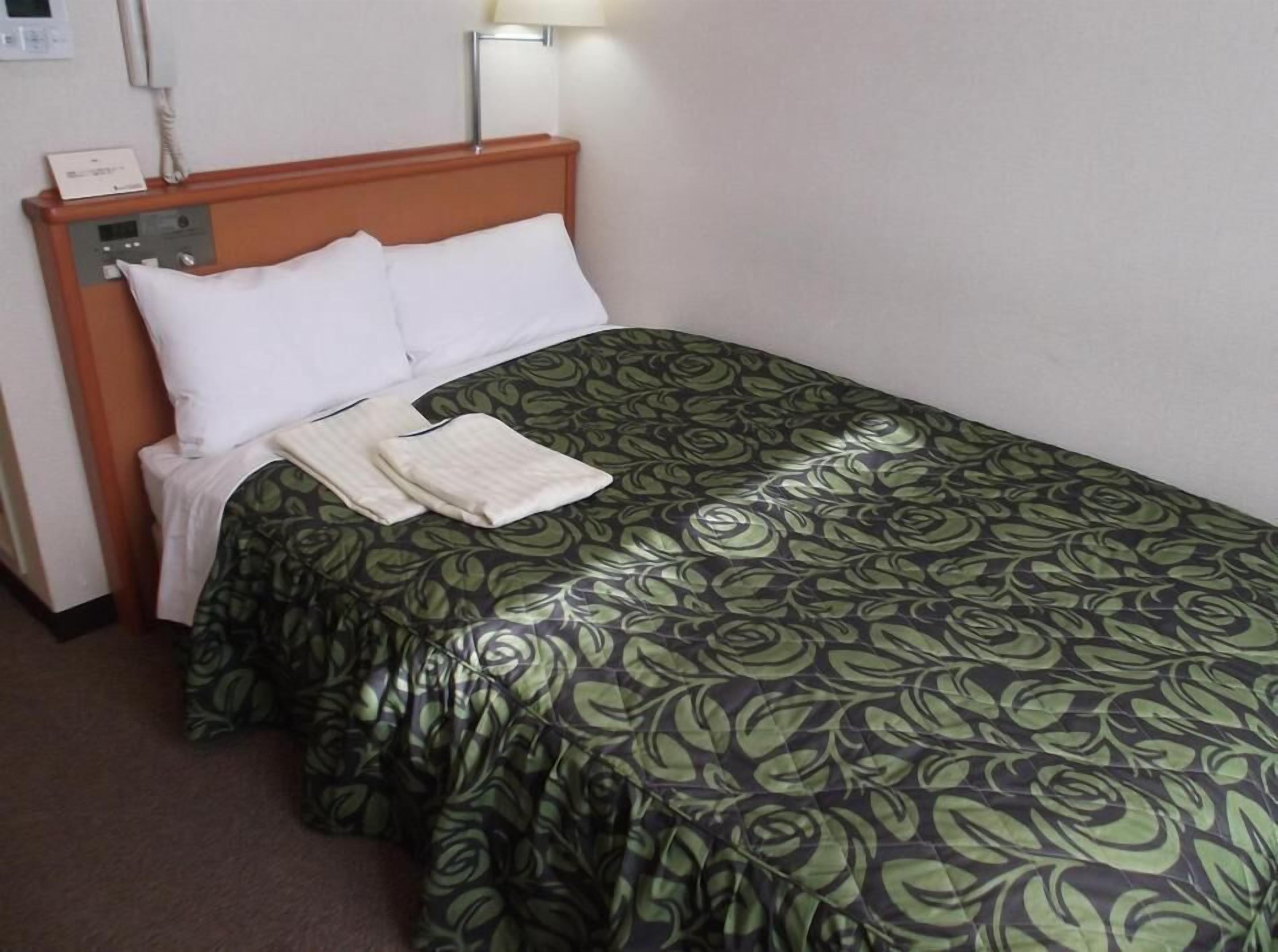 Ein Hotelzimmer mit Bett, Nachttisch, Lampe und einem an der Wand befestigten Telefon.