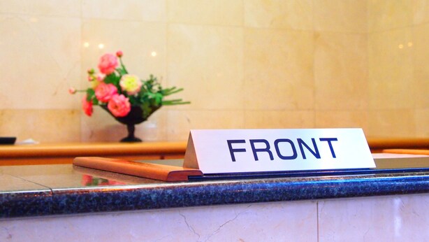 A reception desk with a sign that reads "SUNRISE 21" and a "FRONT" sign on a marble counter. - Hotel Sunrise 21 (Higashihiroshima)