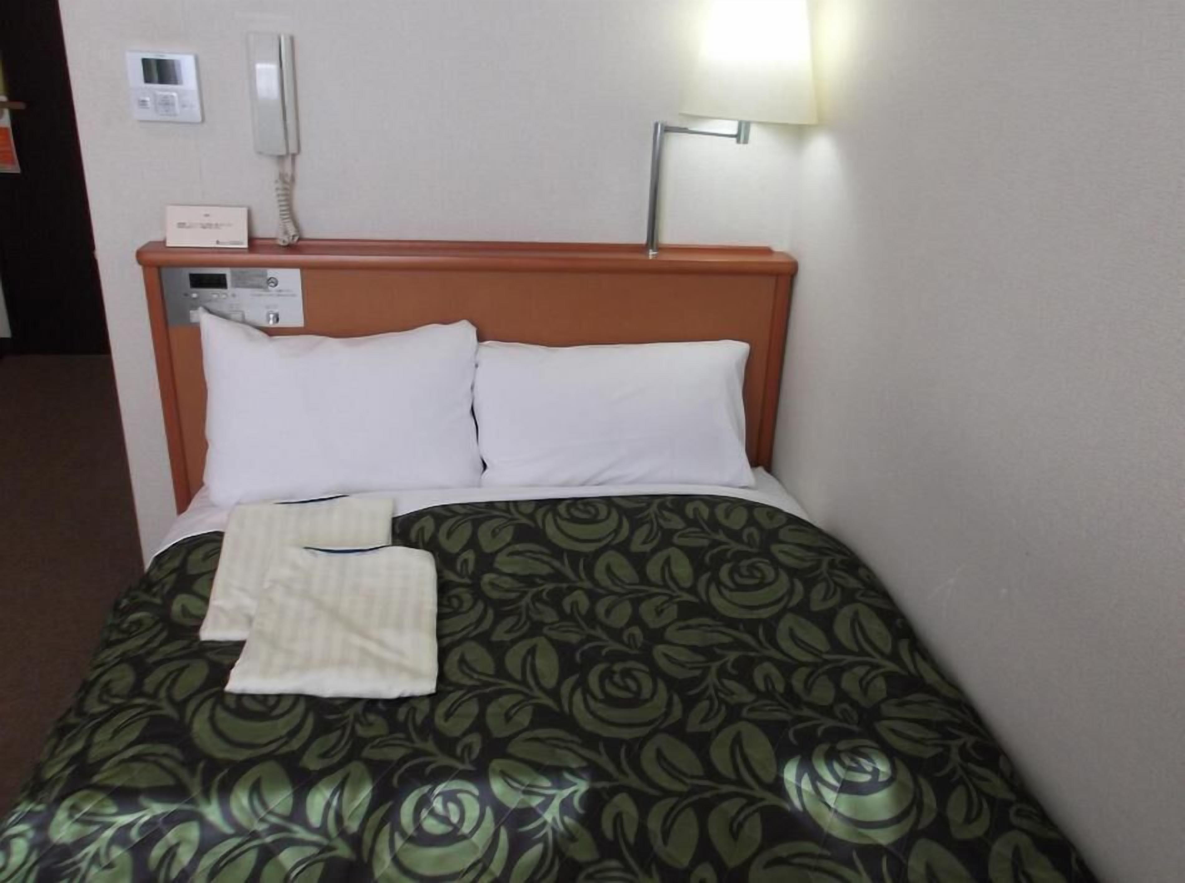 Ein Hotelzimmer mit einem Bett, einem Nachttisch mit Lampe, einem Telefon und einem Thermostat.