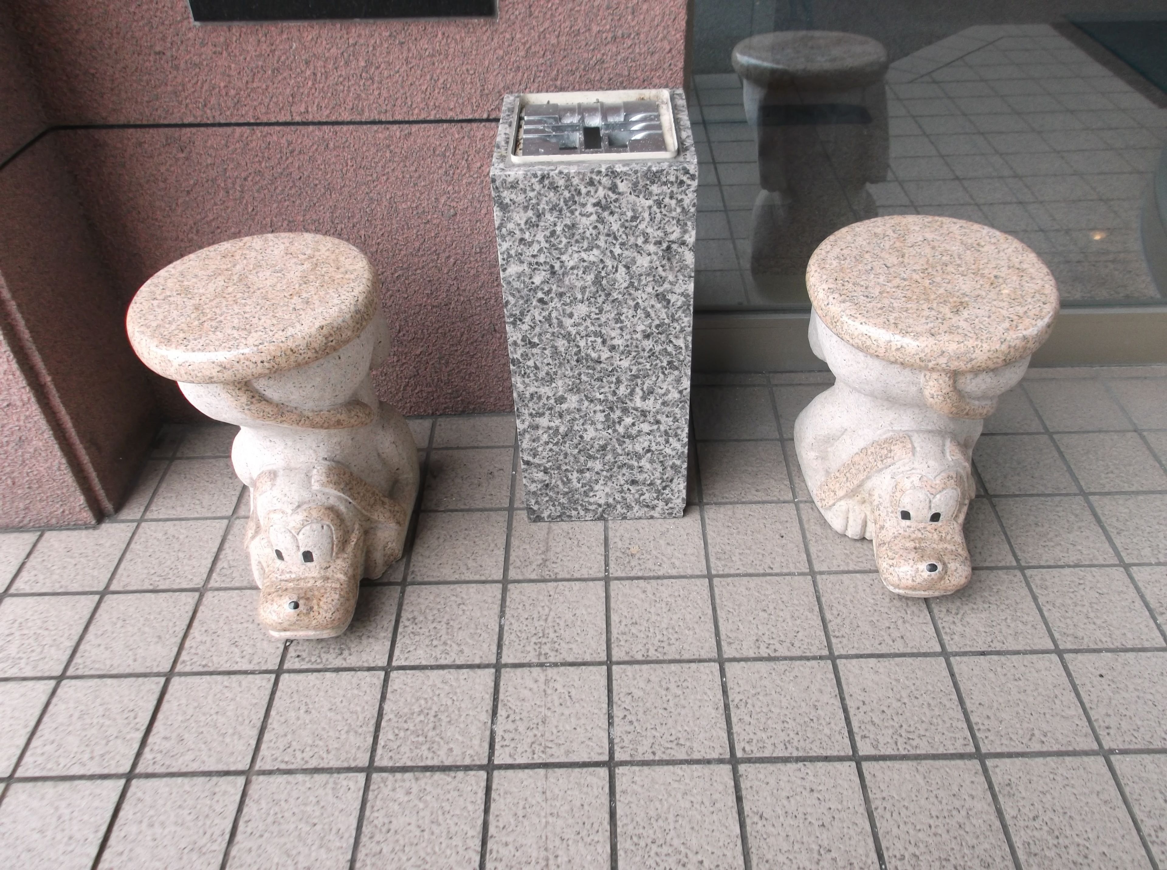 Two toilets with animal-shaped seats and a granite pedestal in a tiled area.